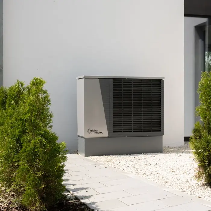 An air source heat pump outside a modern house between two shrubs